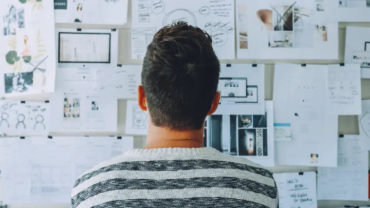 Man thinking while looking at a wall with paper on it.