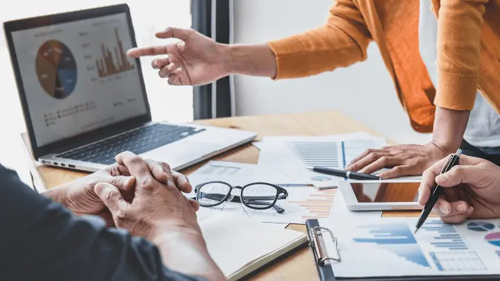 Three people in a meeting, one is presenting data using a laptop