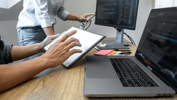 Two people looking at website code on desktop and laptop