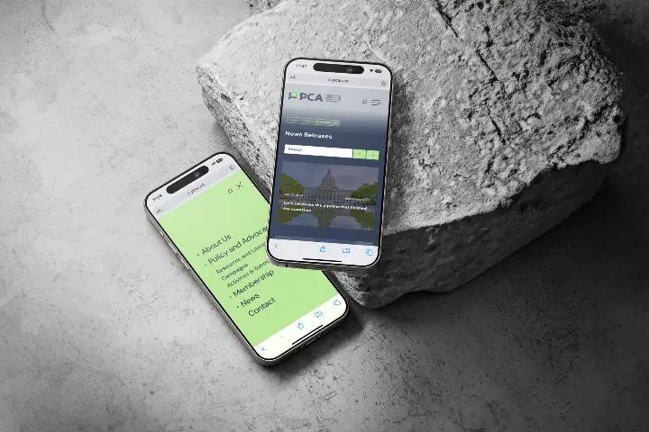 Two smartphones showing PCA's website, one smartphone is on a rock, the other is on the ground.